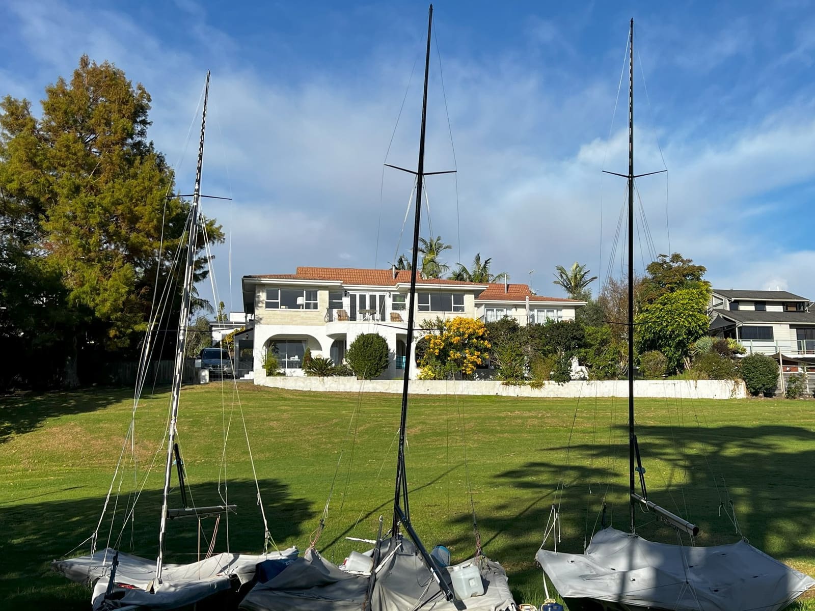 Das weiße Haus am Hügel — Waiake Beach Apartments von der Aickin Reserve aus gesehen, davor die Segeljollen des Clubs