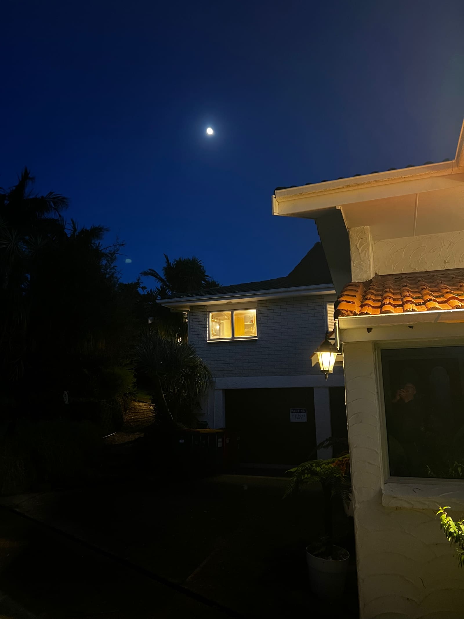 The house at dusk with the moon above and a light in the window