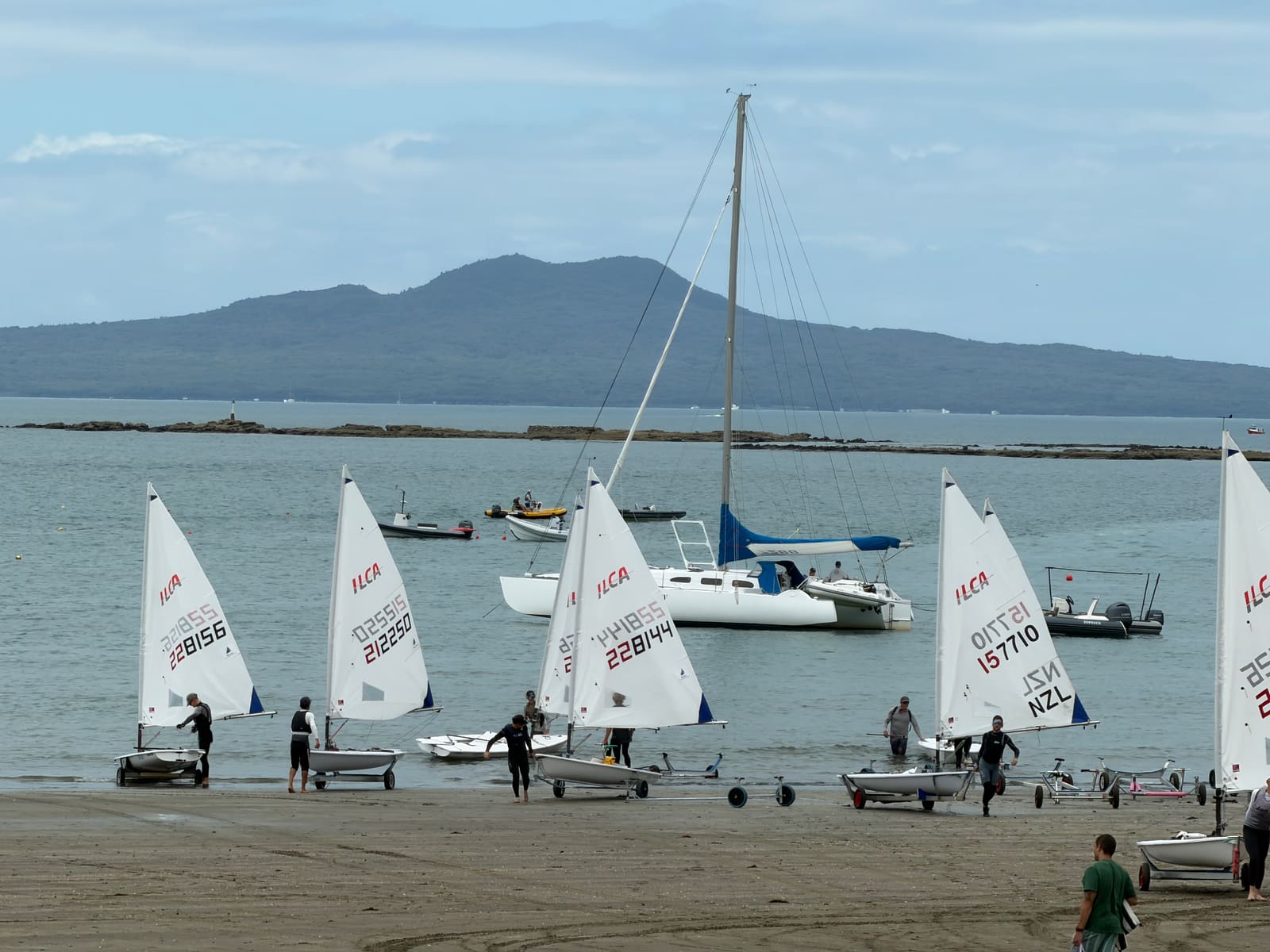 ILCA dinghies launching off Waiake Beach with Rangitoto behind